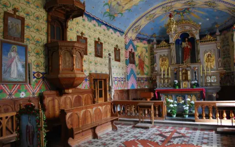 Wnętrze kościoła w Bukowinie Tatrzańskiej. Drewniana ambona, ławy i ołtarz zdobią kolorowe malowidła.