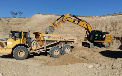 Excavadora CAT cargando volquete Volvo en obra de movimiento de tierras.