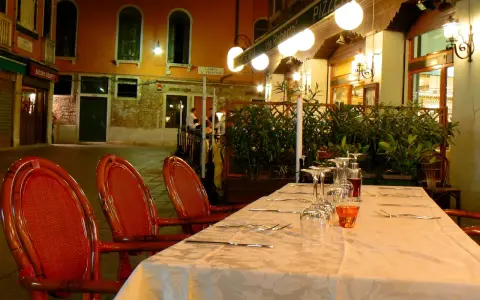 Table dressée devant la trattoria "da Roberto" à Venise, avec des chaises rouges et des verres à vin.