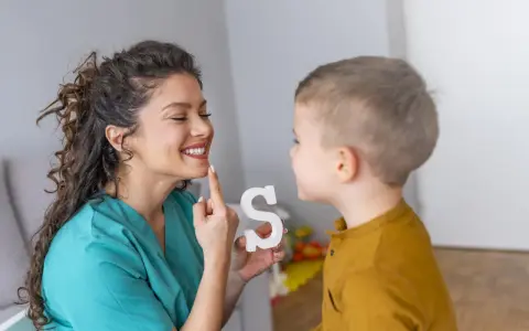 Logopeda pomaga dziecku z dyslalią ćwiczyć wymowę litery "S", używając białej literki.