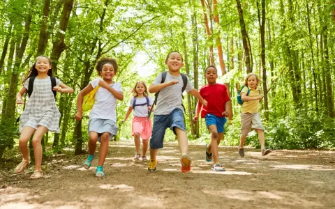 Des enfants joyeux, des supernova juniors, courent sur un sentier forestier ensoleillé, pleins d'énergie.