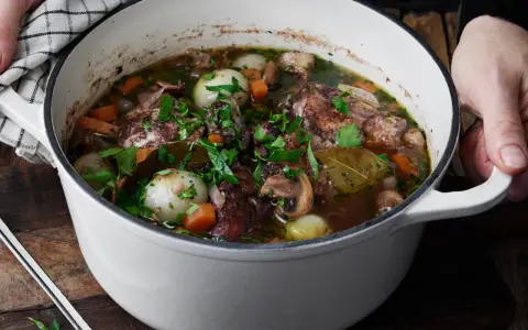 En gryta med mustig coq au vin, fylld med möra kycklingbitar, champinjoner, lök och morötter, toppad med färsk persilja.