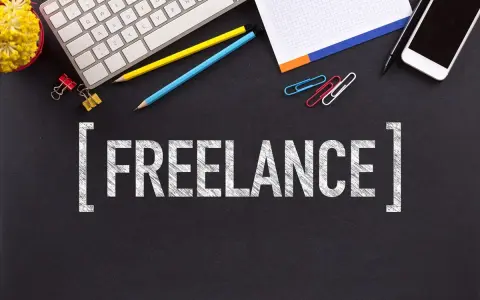Biurko z klawiaturą, telefonem i napisem "FREELANCE". To styl pracy, gdzie pracujesz dla różnych klientów, sam ustalając godziny.