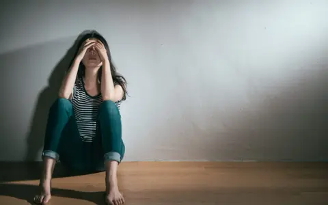 En kvinna sitter på golvet med händerna över ansiktet, en bild som symboliserar grov depression och ensamhet.
