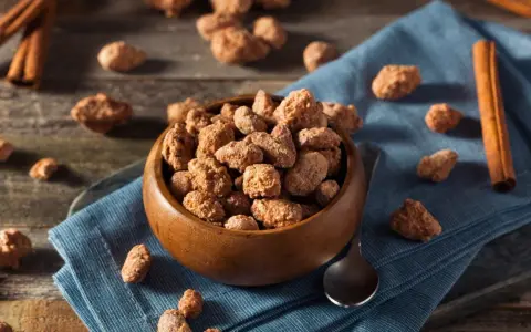 Schüssel mit gebrannten Mandeln, Zimtstangen und Löffel. Ein süßer Snack, der auch in der Schwangerschaft genossen werden kann.