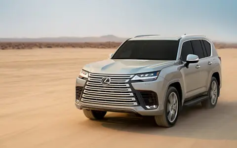 Srebrny Lexus LX 600 przemierza pustynię, zostawiając ślady na piasku.