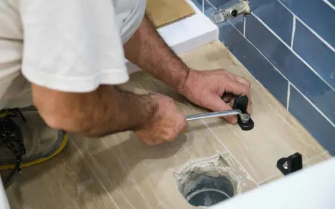 A person uses a wrench to tighten a toilet flange bolt, demonstrating how to replace a toilet flange.