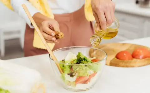 Kobieta dodaje oliwę do sałatki, przygotowując posiłek zgodny z dietą South Beach.
