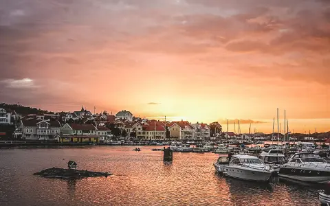 En pittoresk svensk kuststad vid solnedgången, med båtar i hamnen och hus längs vattnet. En perfekt plats för upplevelser i Sverige.