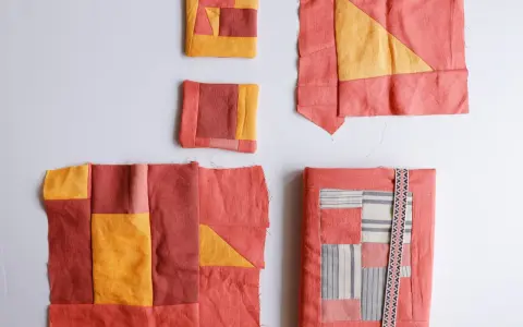 Kilka fragmentów tkanin w odcieniach koralu i żółci, tworzących wzory geometryczne. To jest właśnie patchwork – sztuka łączenia skrawków materiału.