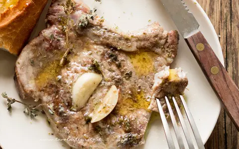 Succulenta braciola di maiale condita con aglio e erbe aromatiche, servita con pane croccante.