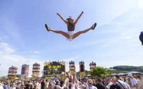 Eine Frau macht einen Spagat in der Luft vor einer Bühne bei einem der Festivals NRW. Die Menge jubelt.