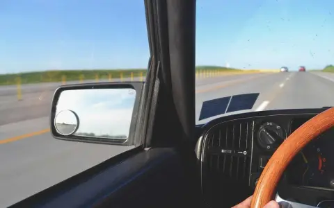Widok z wnętrza samochodu jadącego po pustej drodze. Kierownica, deska rozdzielcza i lusterko boczne. Pomyśl o tym, jak odzyskać zabrane prawo jazdy za alkohol na 3 lata.