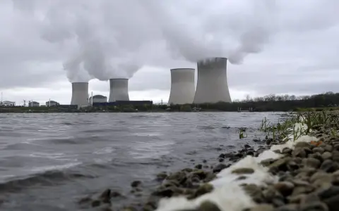Kühltürme eines Atomkraftwerks mit Dampfschwaden über einem Flussufer.
