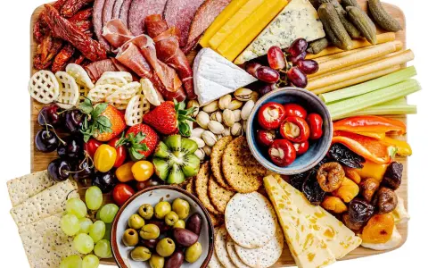 En generös bricka med kall mat: salami, skinka, ostar, oliver, frukt, grönsaker och kex. Perfekt för en festlig tillställning.