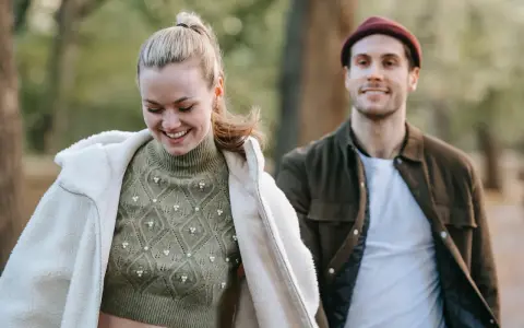 Ein lächelndes Paar im Freien. Sie trägt einen Strickpullover und eine Lammfelljacke, er eine Jacke und Mütze. Perfekt, um was anziehen bei 15 Grad.