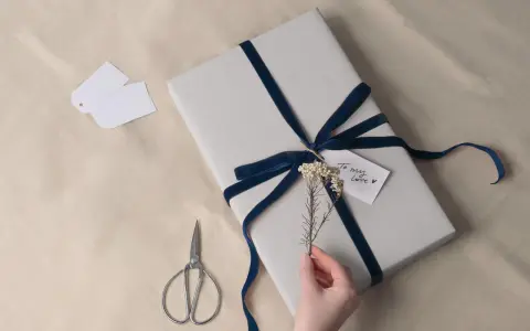 Prezent na 8 rocznicę ślubu, owinięty w szary papier i ozdobiony granatową aksamitną wstążką. Drobna gałązka i karteczka "To my love" dodają uroku.