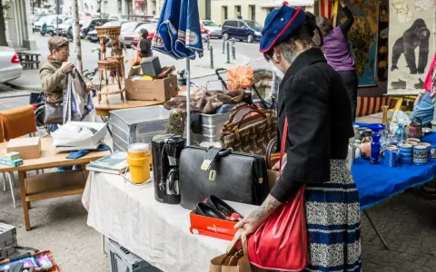 Frau mit Tätowierungen auf dem Arm sucht auf einem antik flohmarkt nach Schätzen. Sie hält eine rote Tasche.