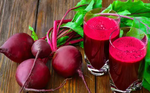 Frische rote Bete und zwei Gläser mit leuchtend rotem Rote-Bete-Saft stehen auf einem Holztisch.