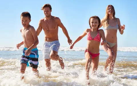 Famiglia corre felice nel mare del lido di Savio, spruzzi d'acqua e sole.