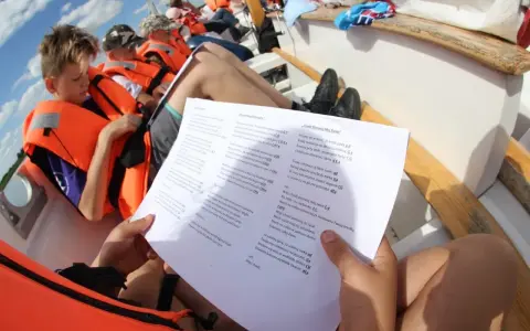Dzieci na łodzi z kamizelkami ratunkowymi śpiewają piosenki żeglarskie dla dzieci.