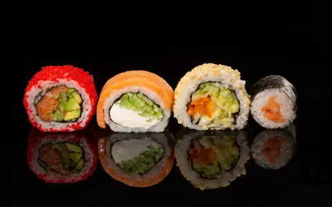 Różne rodzaje sushi: rolka z łososiem i awokado w ikrze, z łososiem i serkiem, z sezamem i warzywami, oraz klasyczne maki z łososiem.