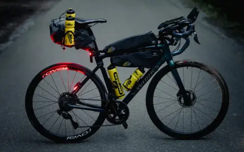 Bereit für ultra cycling: Rennrad mit Bikepacking-Taschen, Trinkflaschen und Lichtern auf asphaltierter Straße.
