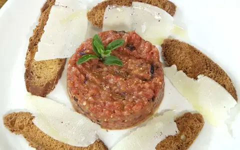 Delicioso tartar de tomate fresco, servido con finas láminas de queso y tostadas crujientes.