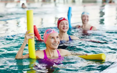 Kobiety w czepkach pływackich ćwiczą w basenie z makaronami. To ich urlop dla poratowania zdrowia, pełen uśmiechu i aktywności.