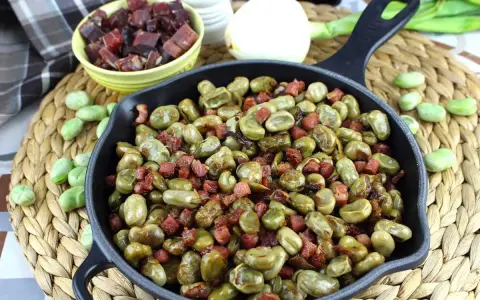 Habas tiernas salteadas con trocitos de jamón en una sartén de hierro fundido, un plato tradicional lleno de sabor.