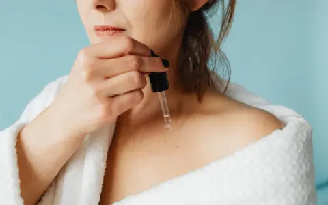 Une femme applique un sérum à base de peptide sur sa peau, enveloppée dans un peignoir blanc douillet.