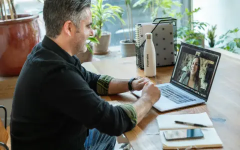 Mann gibt online Nachhilfe. Er lächelt und spricht mit einer Frau auf seinem Laptop.