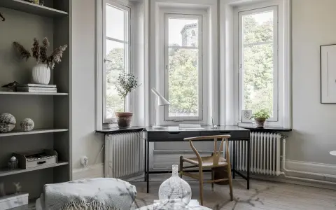 Una **scrivania sotto finestra** con vista sul verde. Un angolo studio accogliente con piante, lampada e una sedia di design.
