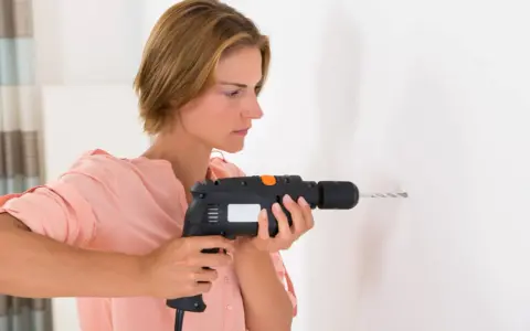 Mujer usando un taladro, mostrando sus partes como el gatillo y la broca, para hacer un agujero en la pared.