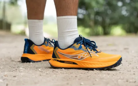 Gambe di persona che indossa scarpe da trail running Saucony arancioni e blu su un sentiero sterrato.