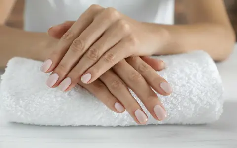 Dłonie z idealnym, jasnoróżowym manicurem kombinowanym spoczywają na białym ręczniku.