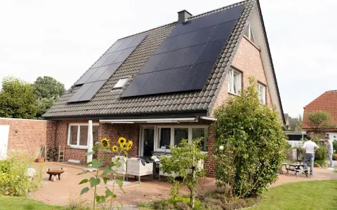 Tak på ett tegelhus med solceller som ger hög verkningsgrad. Solrosor blommar på uteplatsen.