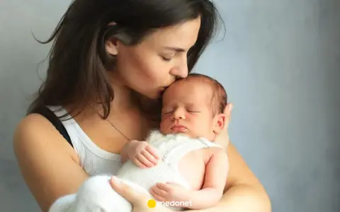 Matka całuje śpiące dziecko, które może cierpieć z powodu gazów u noworodka.