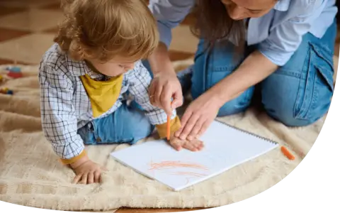Ein Kind malt mit einem Wachsmalstift auf einem Blatt Papier, während eine Erwachsene ihm hilft. So können sie kinder motivieren mitzumachen.