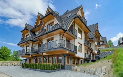 Nowoczesne apartamenty Bachledzki Wierch z drewnianymi elementami i balkonami, otoczone zielenią.
