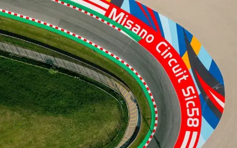 Vista aerea del circuito di Misano, con la scritta "Misano Circuit Sic58" in rosso e un disegno colorato.