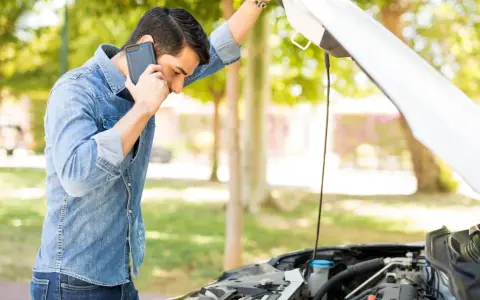 Mann telefoniert neben offenem Motorraum. Was ist beim Abschleppen zu beachten bei PKW Defekt?