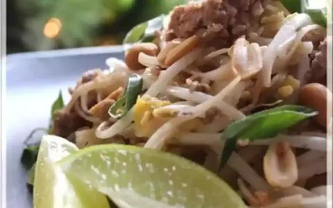 Délicieux pad thai porc avec pousses de soja, cacahuètes et quartiers de citron vert.