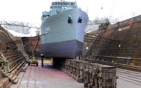 Un grand navire est en cale sèche, soutenu par des structures en bois. Le support bateau cale sèche est essentiel pour les réparations.
