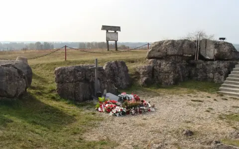 Pomnik na Górze Strękowej z krzyżem i wieńcami. W tle widoczne bunkry i krajobraz.