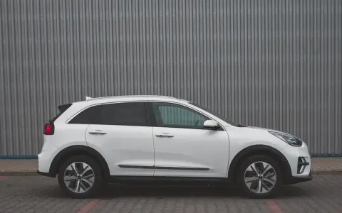 Biały Kia Niro EV widziany z boku na tle szarej, falistej ściany.