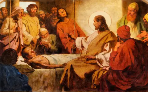 Jesus with a halo touches a sick man lying in bed, surrounded by onlookers.