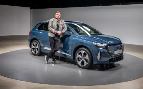 Ein Mann lehnt lässig an einem blauen Audi Q4 e-tron 2026.