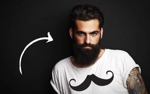 Hombre con barba tupida, quizás decidiendo dejarse barba por primera vez. Camiseta blanca con estampado de bigote.