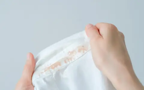 Dłonie trzymają białą koszulę z widoczną, starą plamą z podkładu na kołnierzyku.